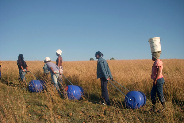 individuals pulling portable water carriers